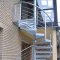 Eine Metallspindeltreppe mit Edelstahlhandlauf als Außenaufgang zu einem geschlossenen Balkon.