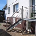 Eine kleinere Metalltreppe mit Stützen und Geländer aus Edelstahl außen an einem Gebäude.