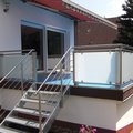 Eine Edelstahltreppe als Aufgang zu einer Terrasse mit Edelstahlgeländer und Milchglasscheiben.
