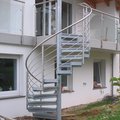 Eine Metalltreppe mit Edelstahlgeländer als Außenaufgang zu einem Balkon mit Edelstahlgeländer und Glasscheiben.